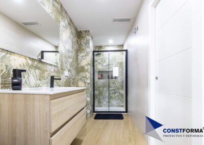 Baño con ducha de perfil negro y mueble de madera